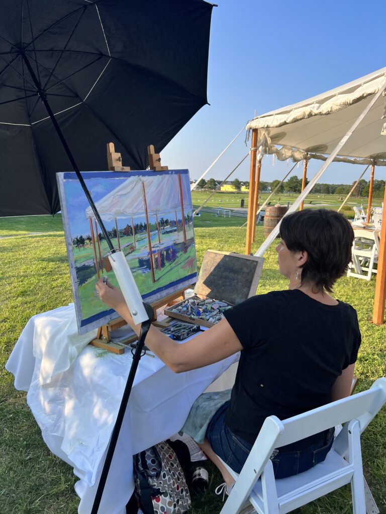a woman sitting at a table with an umbrella painting